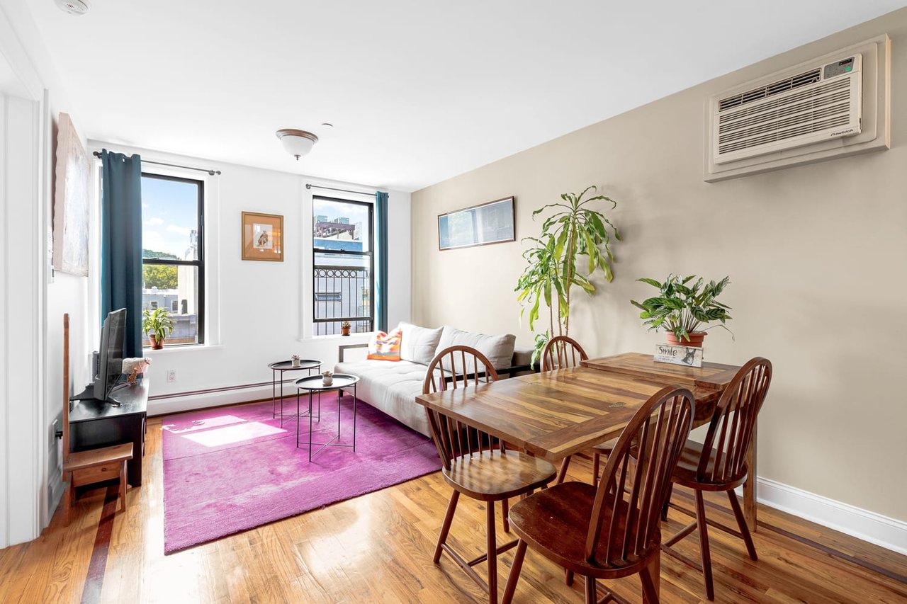 Furnished living and dining area with hardwood floors, magenta rug, and two curtained windows.