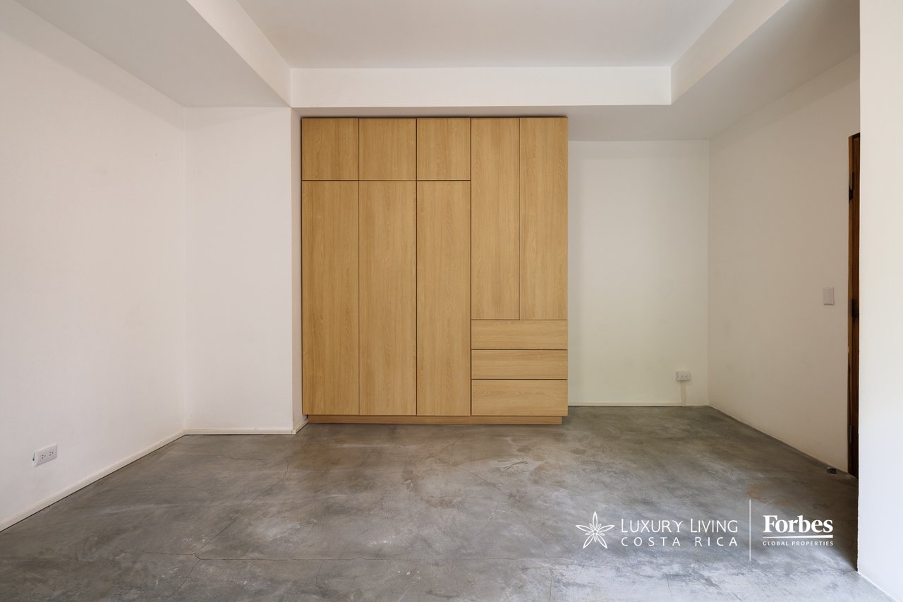 Empty bedroom with a light-wood built-in wardrobe and polished concrete floor.