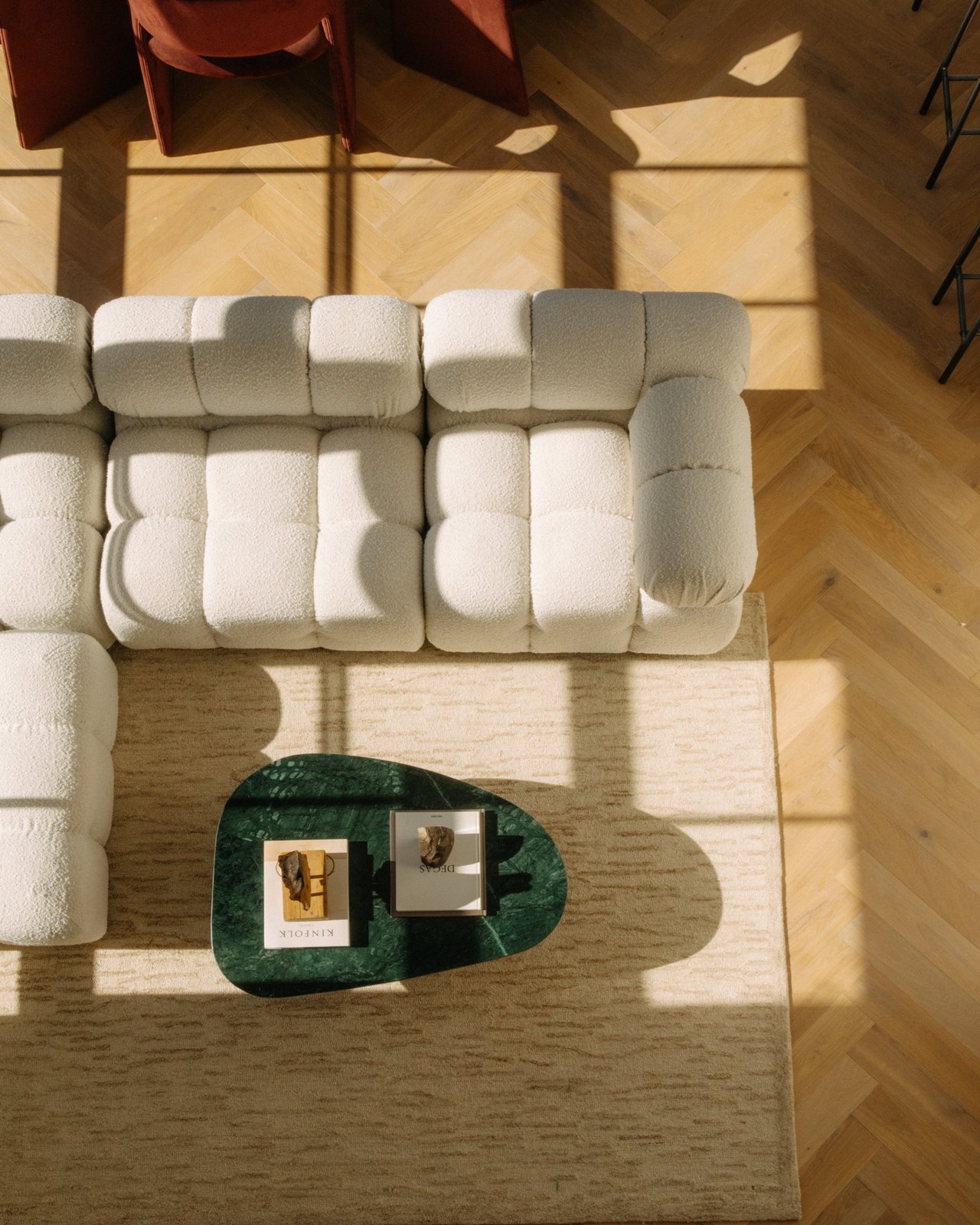 Living room with a cream modular sofa, green stone coffee table, and sunlit herringbone floor.