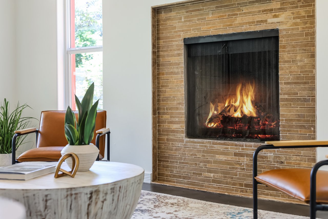 Living room with a lit fireplace, tan tile surround, brown leather chairs, and a round coffee table.