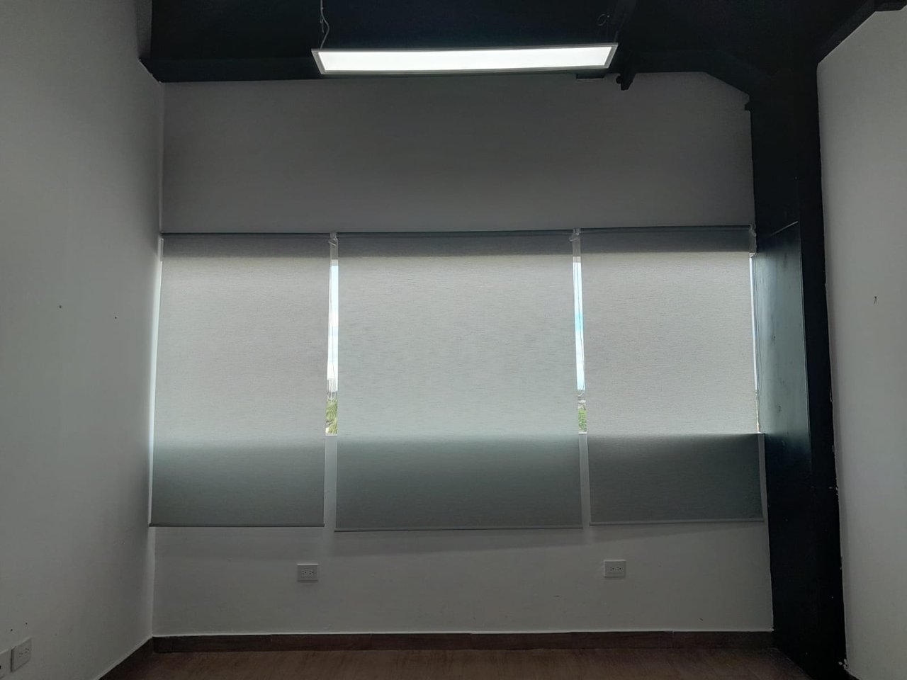 Empty office with shaded windows, an exposed dark ceiling, and wood flooring.
