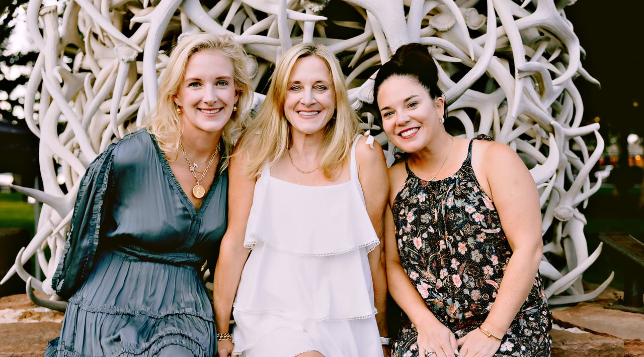 The Legacy Group team, three agents seated together in front of an elk antler arch in Jackson, Wyoming