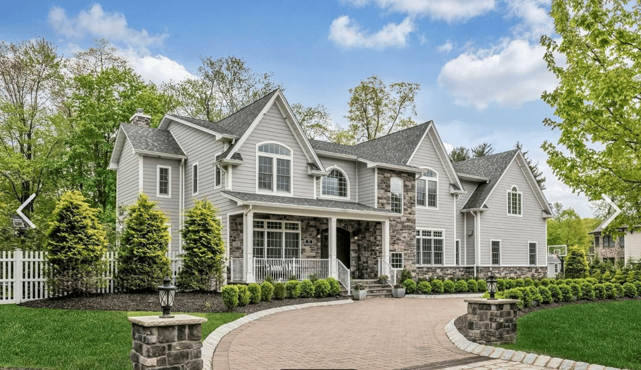 Large gray-sided home with stone accents, a covered porch, and a curved brick driveway.