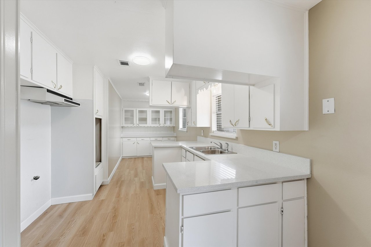 Vacant kitchen with white cabinets, a long peninsula, and light wood-look flooring.