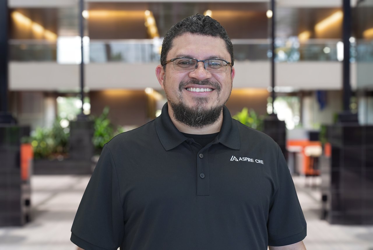 Marlon Estrada smiles in glasses and a black Aspire CRE polo.