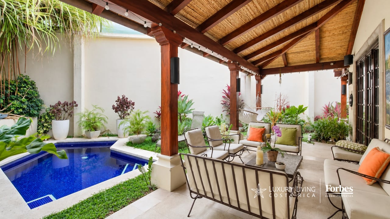 Covered patio with a blue swimming pool, wooden-beam roof, and cushioned seating.