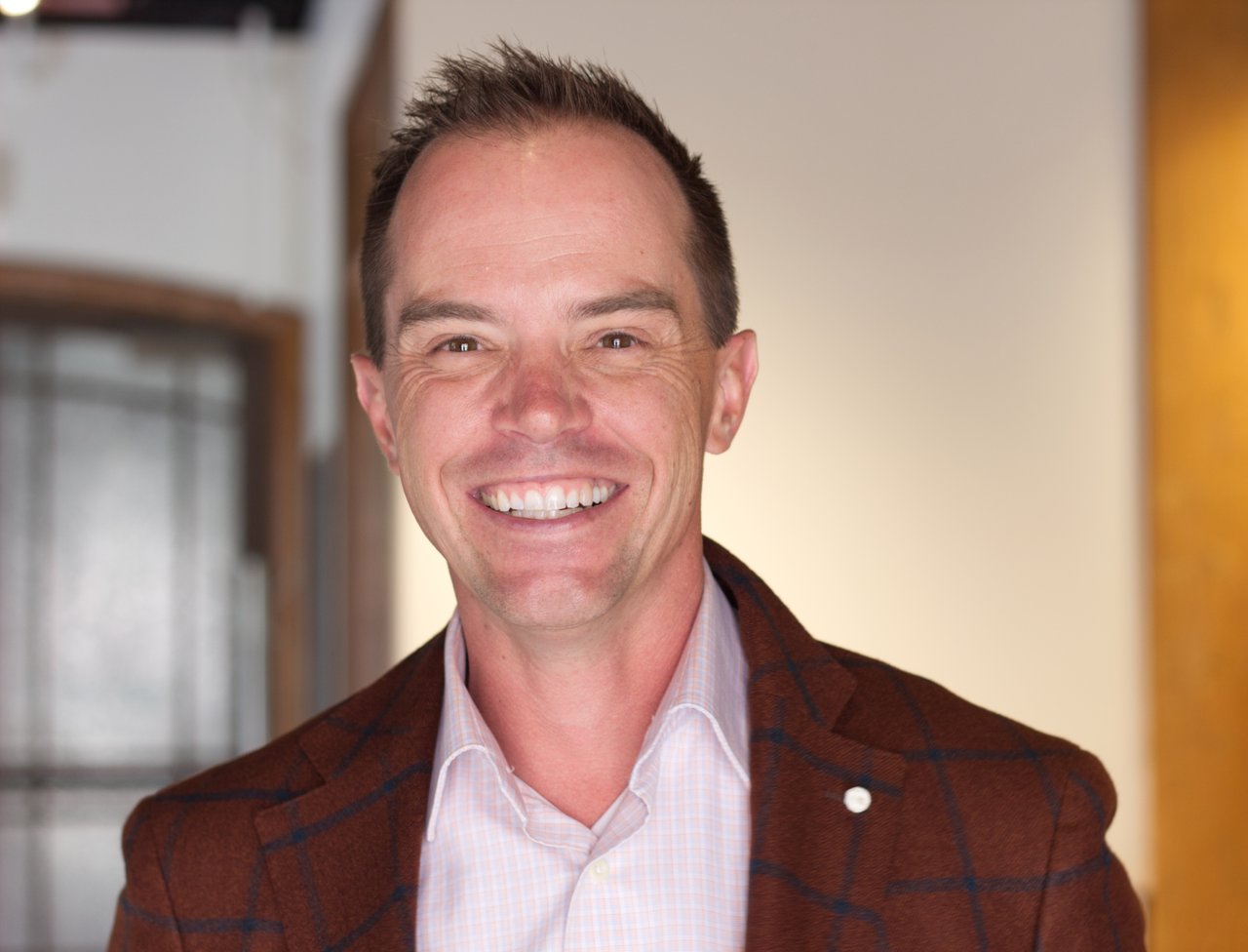 Jared Conlin smiling in a brown plaid blazer and pale checked shirt.