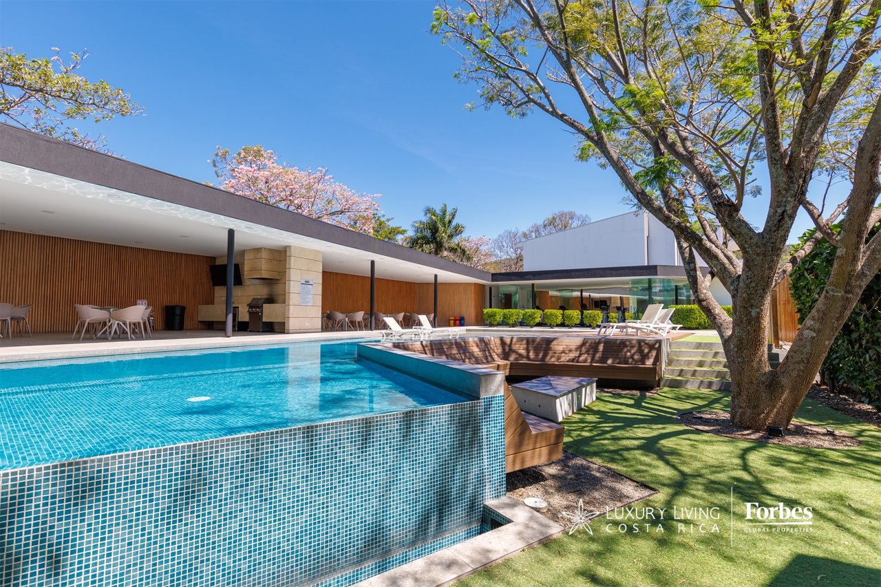 Contemporary home's swimming pool beside a raised wood deck and covered outdoor dining area.
