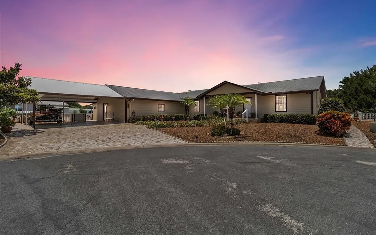 Single-story home with a metal roof, covered carport, and landscaped yard at dusk.