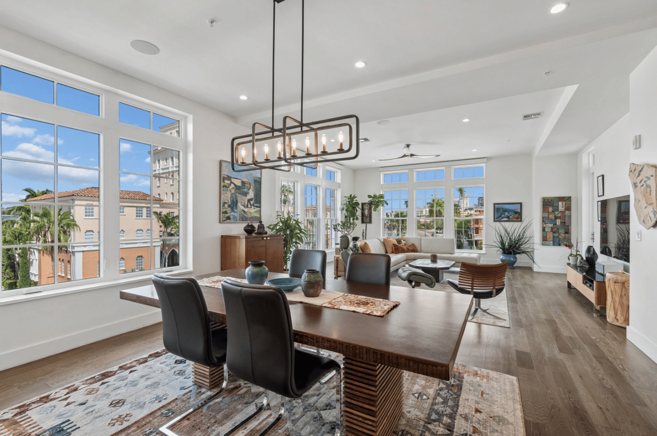 Bright condo living and dining room with tall windows, a large dining table, and a sectional sofa.