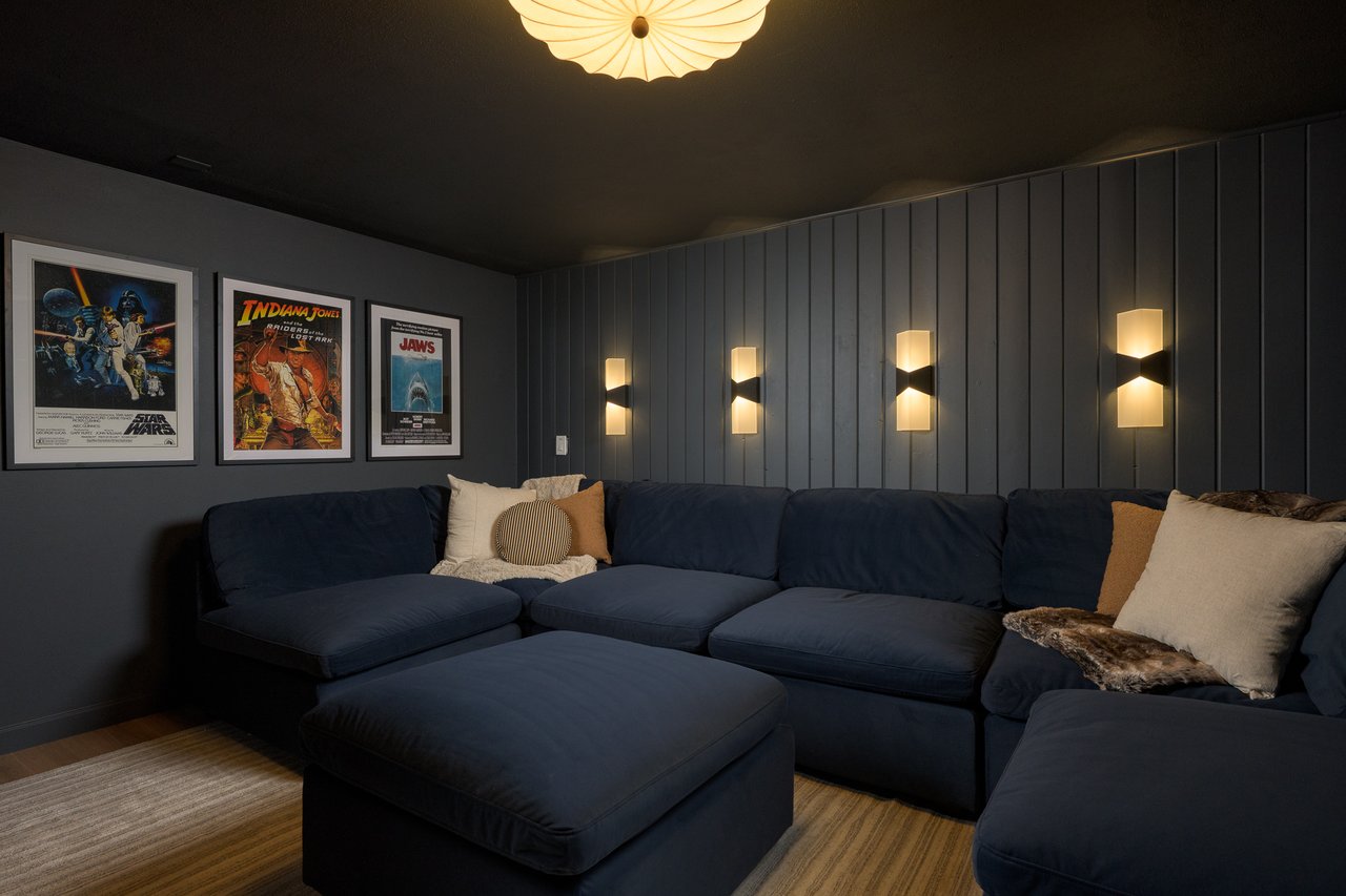 Home theater with a navy sectional, illuminated wall sconces, and framed movie posters.