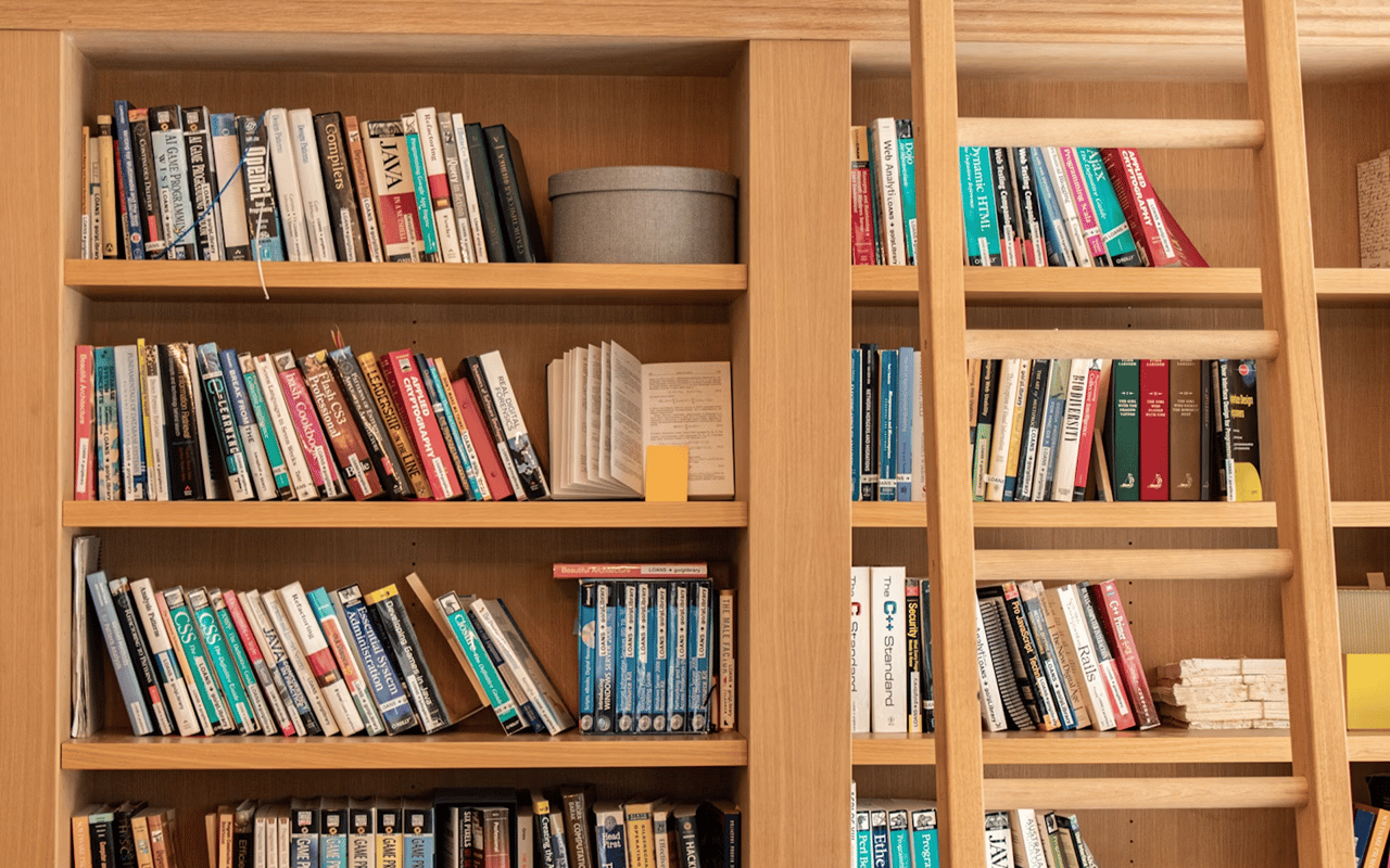 Wooden library bookcases filled with books, with a rolling ladder across the shelves.