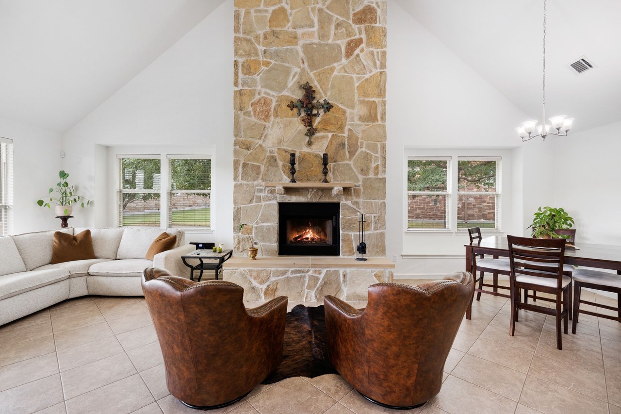 Living room with a tall stone fireplace, vaulted ceiling, cream sectional, and brown leather chairs.