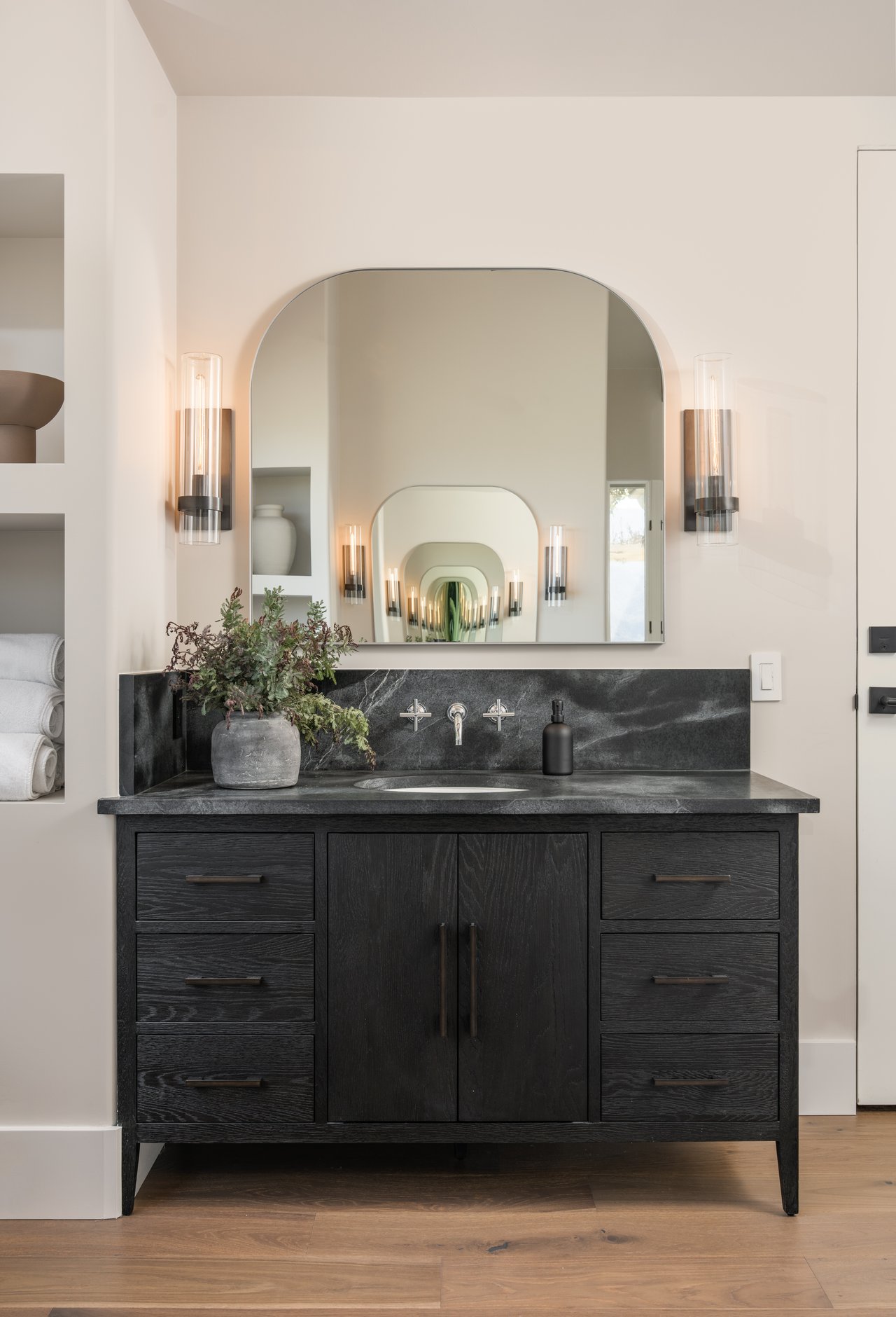 Bathroom vanity with an arched mirror, dark wood cabinetry, and charcoal stone countertop.