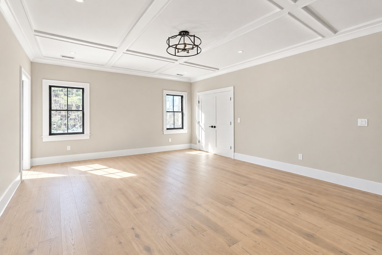 Vacant room with light wood floors, two windows, white double doors, and a coffered ceiling.