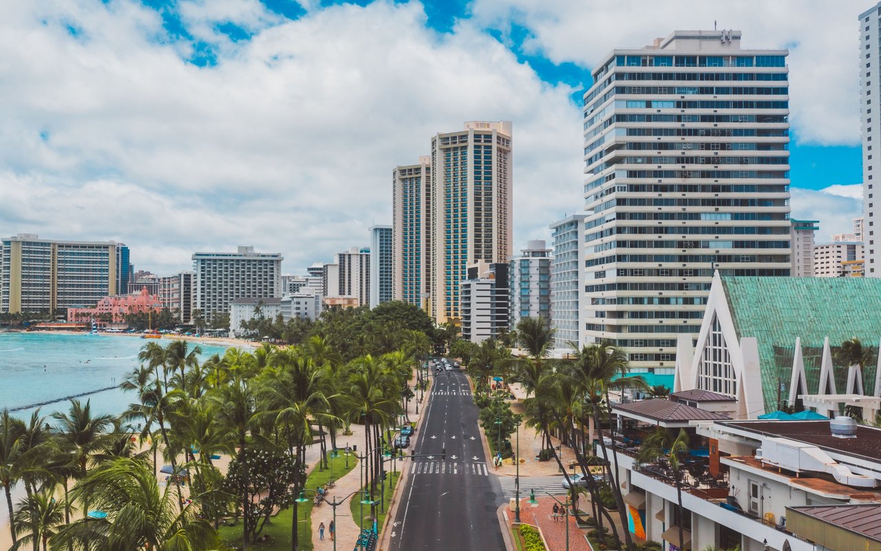 Waikiki beachfront skyline with high-rise hotels, palm-lined shore, and a coastal road.
