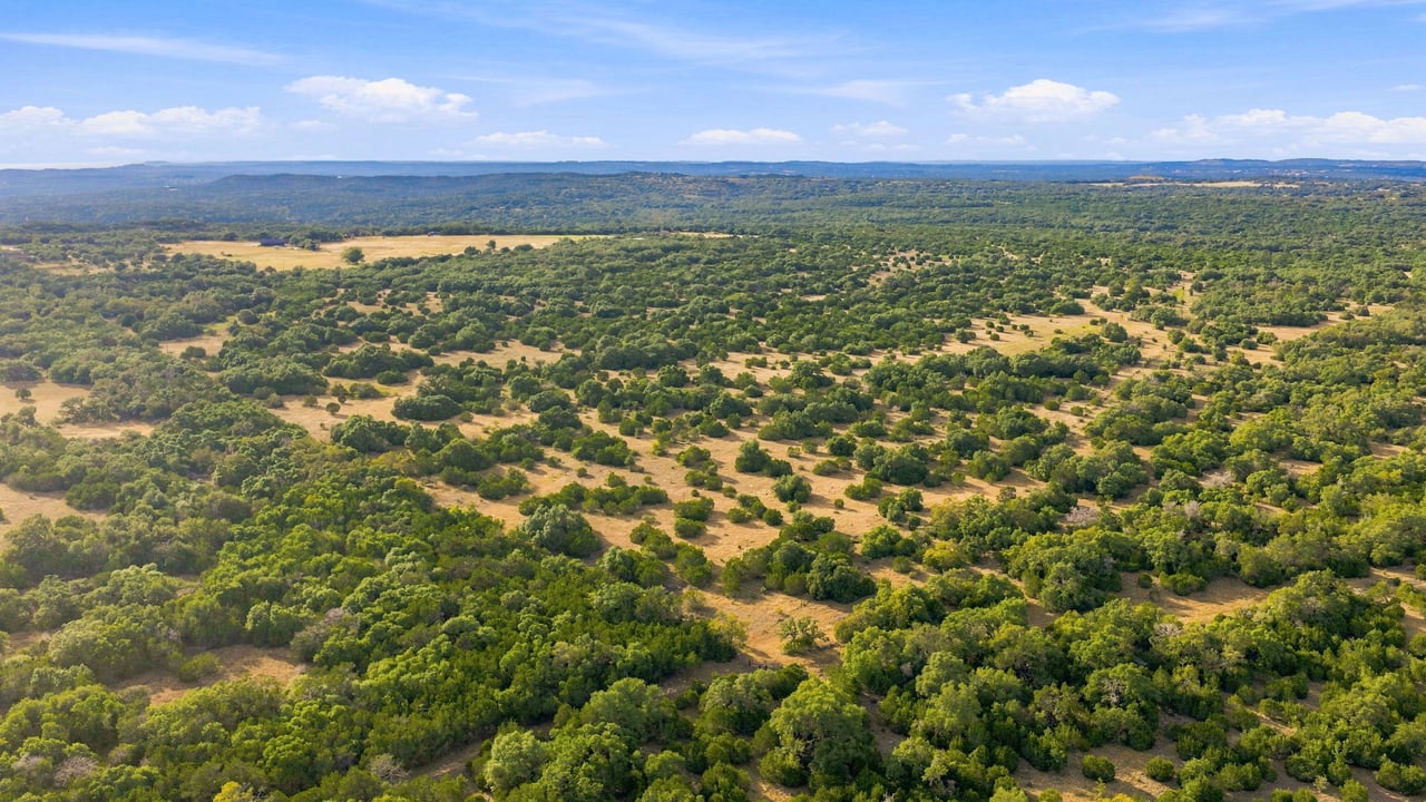 Aerial view of wooded Texas Hill Country ranchland with open clearings stretching to the horizon.