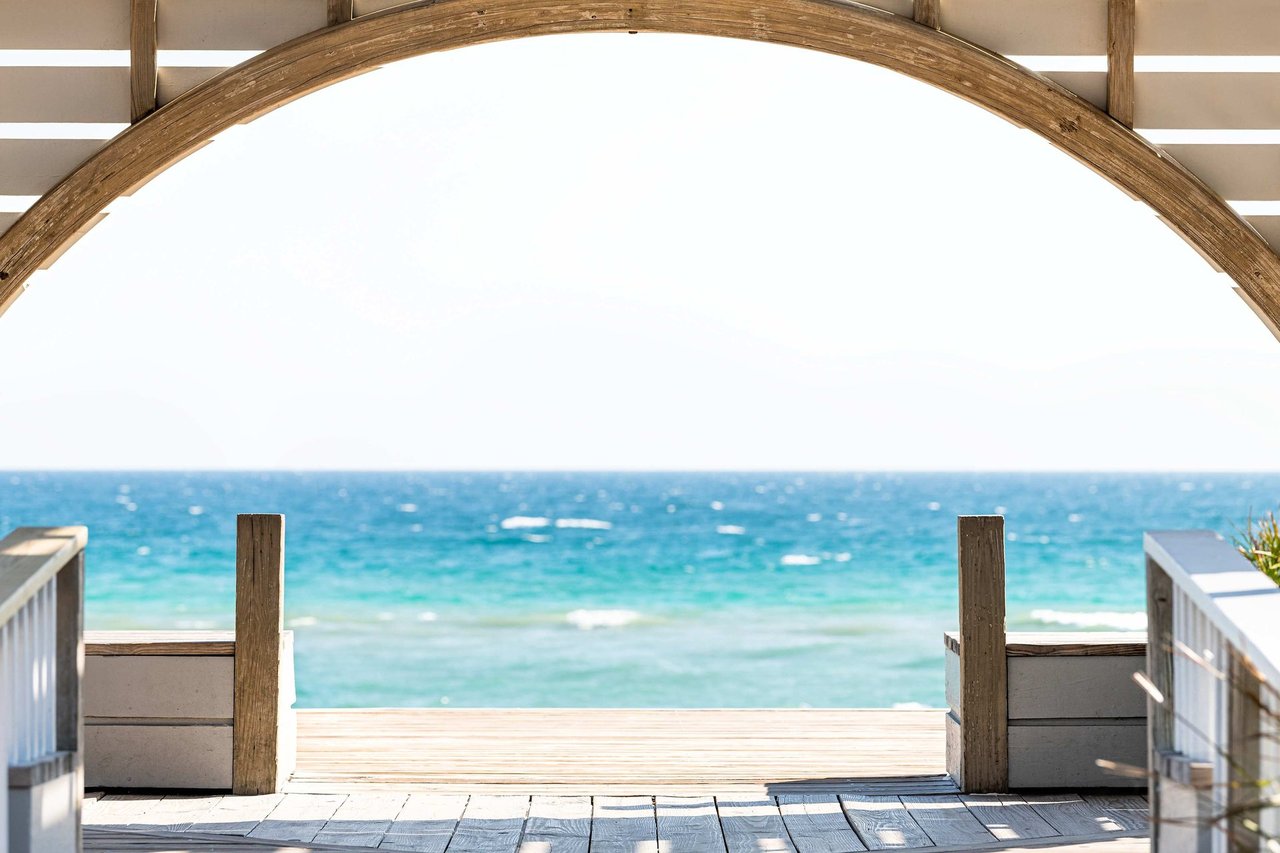 Beachfront deck framed by a wooden arch, overlooking turquoise water.