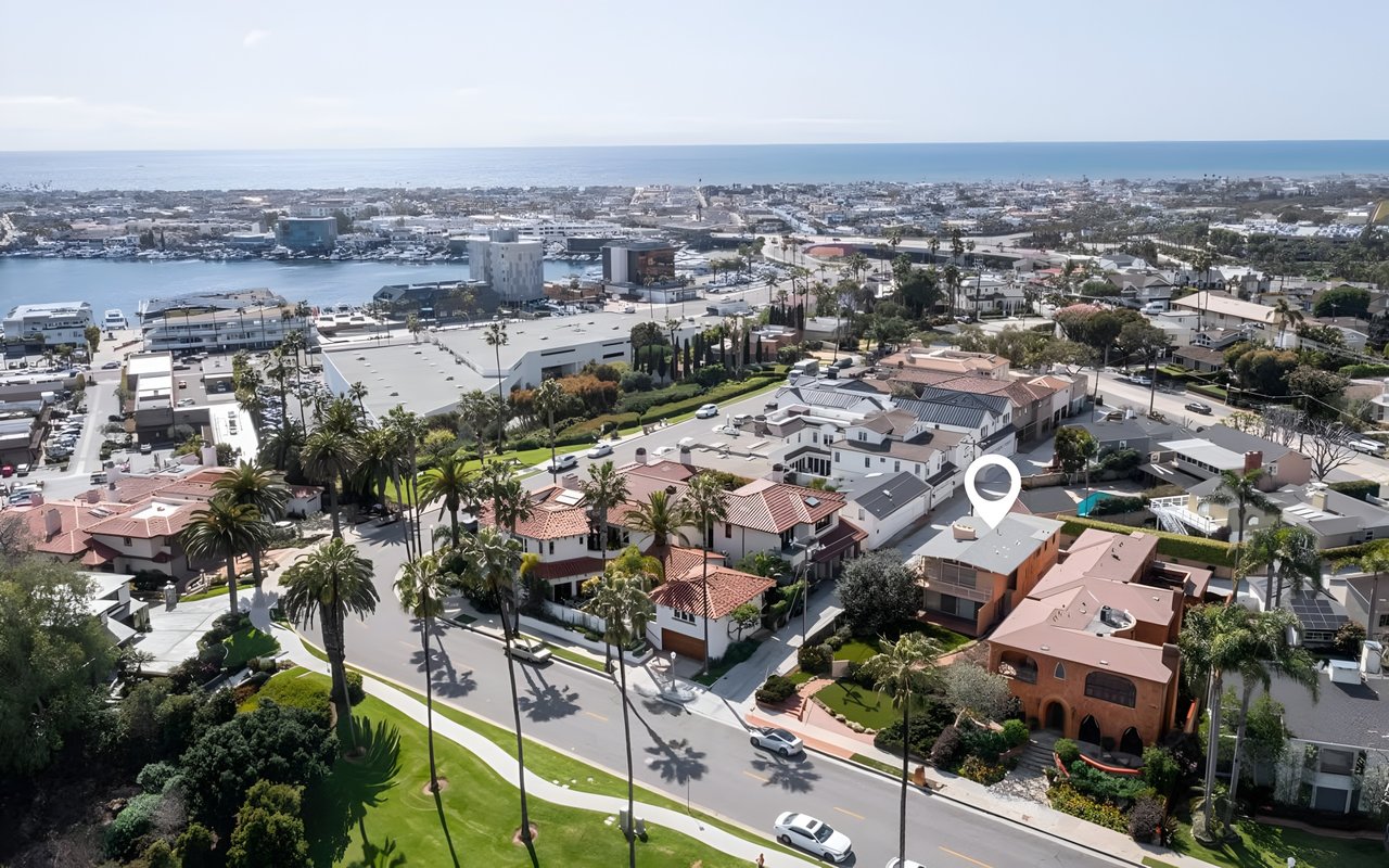  An aerial view of a coastal neighborhood with a white pin marking a house, with a marina and the ocean in the background.