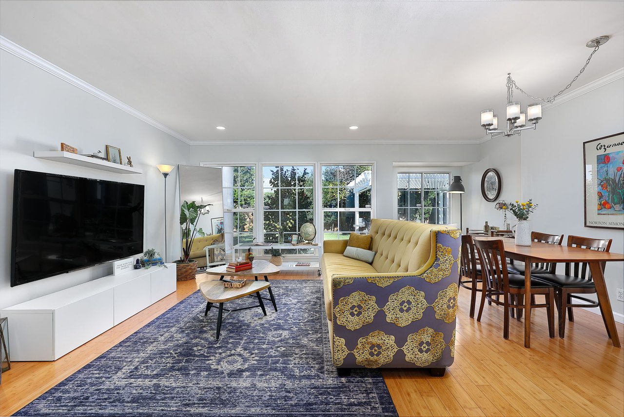 Open-concept living room with bamboo floors, yellow sofa, large TV, and backyard views through large windows