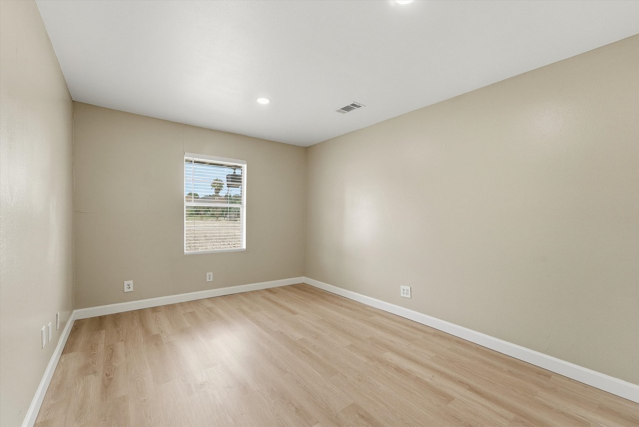 Empty room with light wood flooring and a window with blinds.