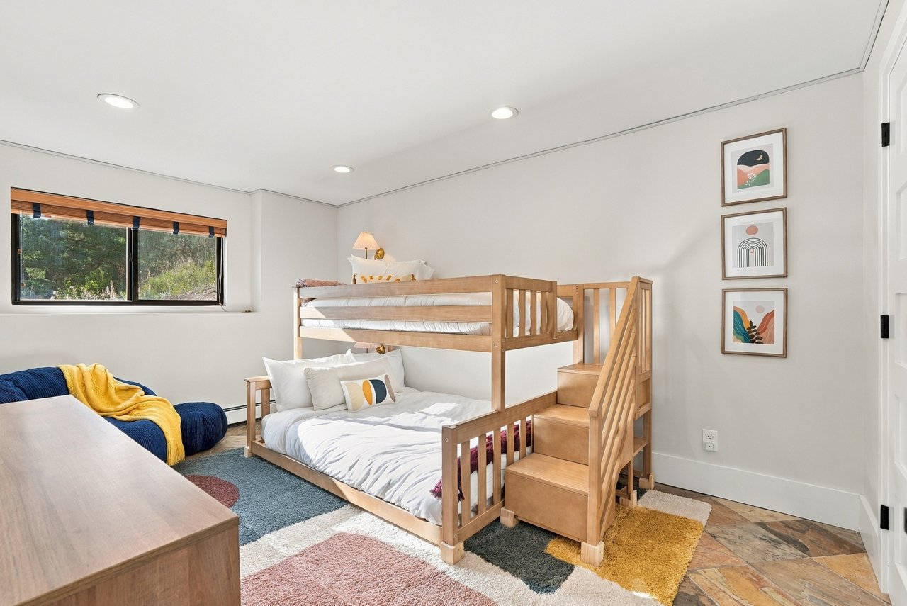 Bedroom with a wooden bunk bed and built-in stairs, colorful rugs, and a navy chair with a yellow throw.
