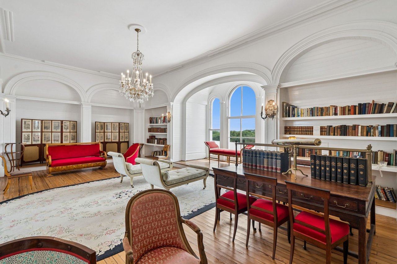 Historic library with arched ceilings, built-in bookshelves, a chandelier, and a large desk by tall windows.