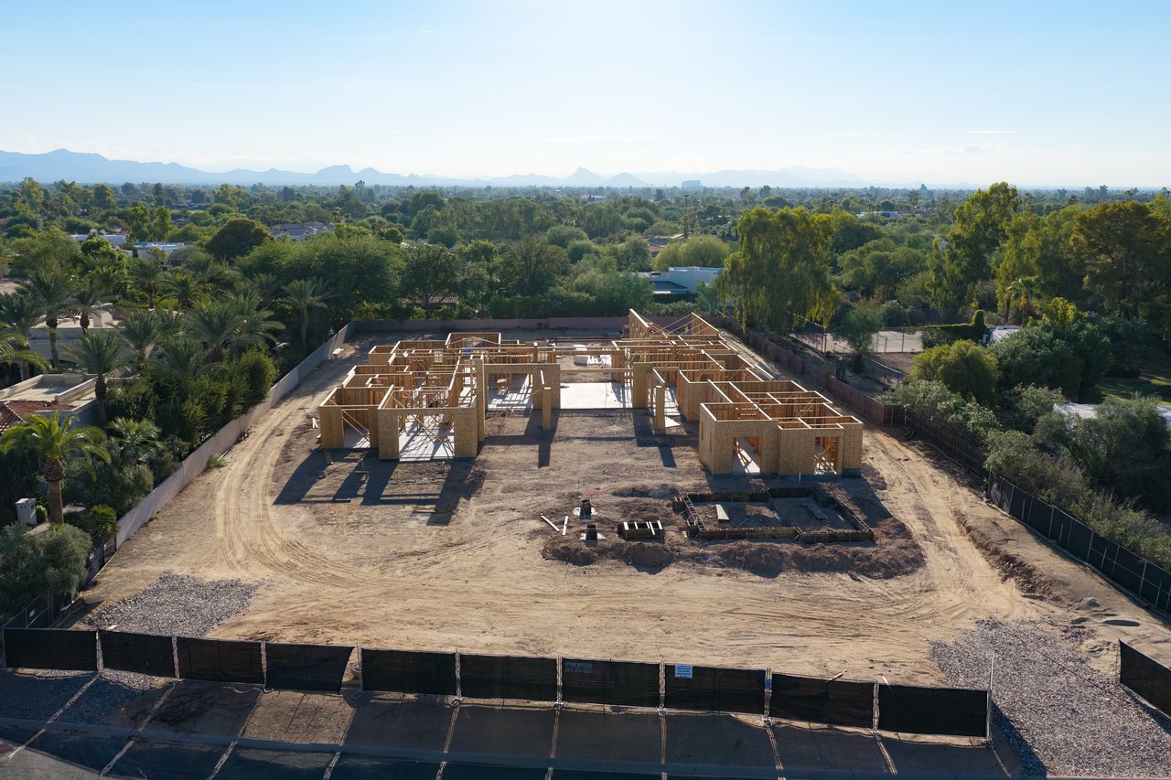Aerial view of a wood-framed home under construction on a cleared lot, with mountains in the distance.