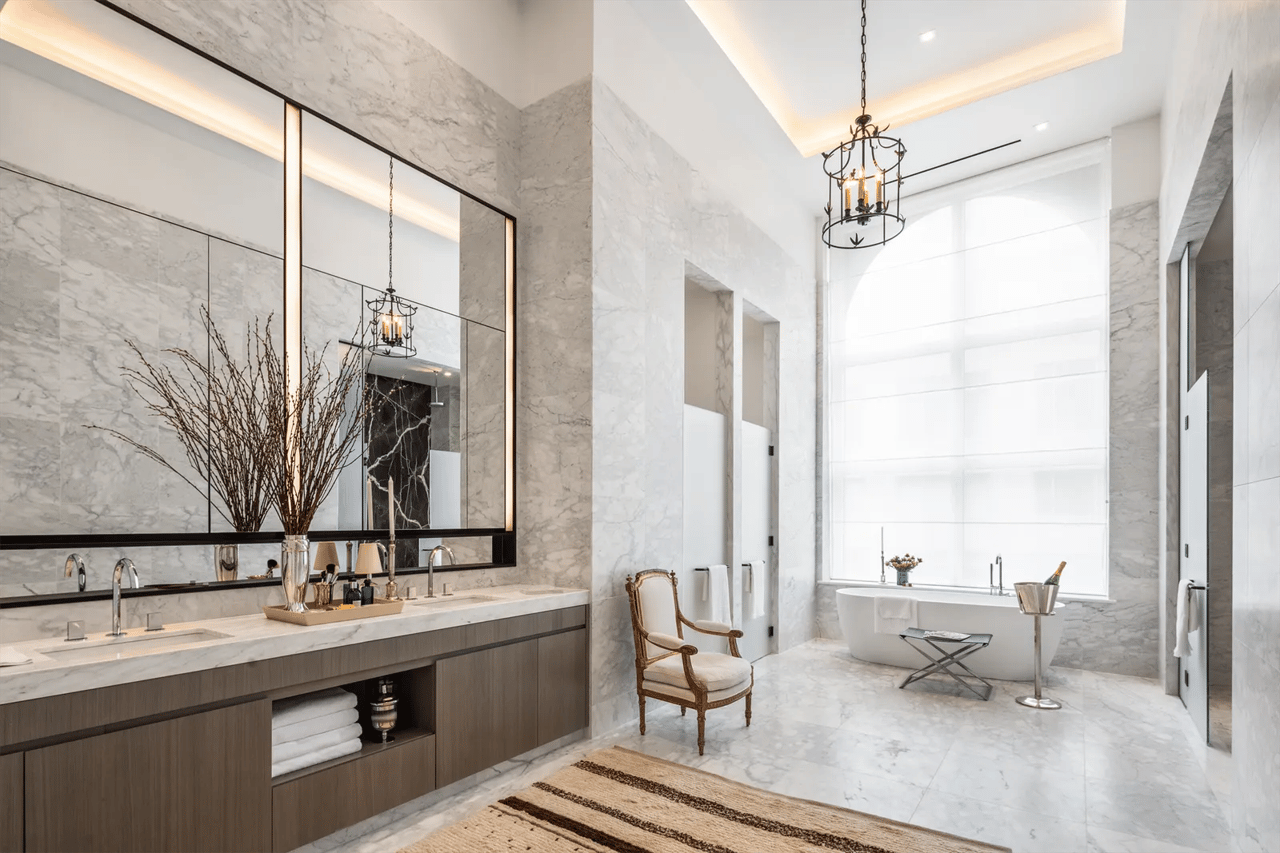 Marble bathroom with a freestanding tub, double vanity, tall window, and chandelier.
