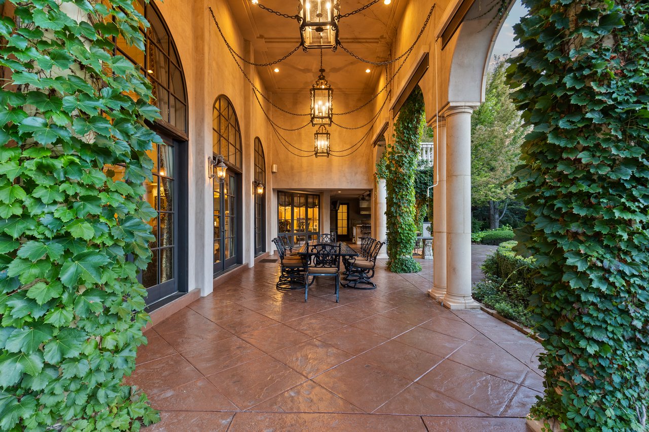 Covered stone terrace with ivy-covered walls, an outdoor dining set, and hanging lanterns.