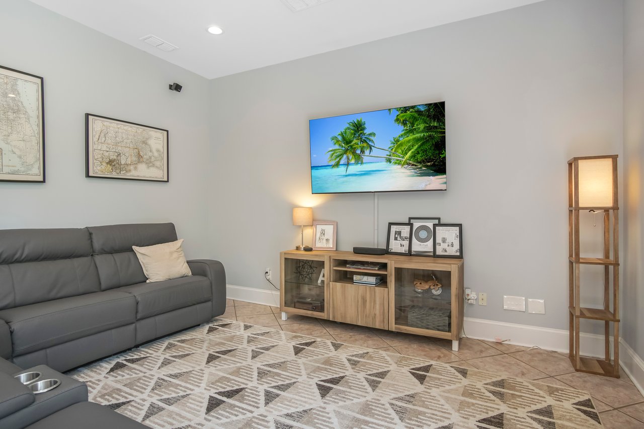 A modern living room with a gray sofa, wooden TV stand, and wall-mounted TV showing a beach scene. Light decor and soft lighting create a cozy atmosphere.