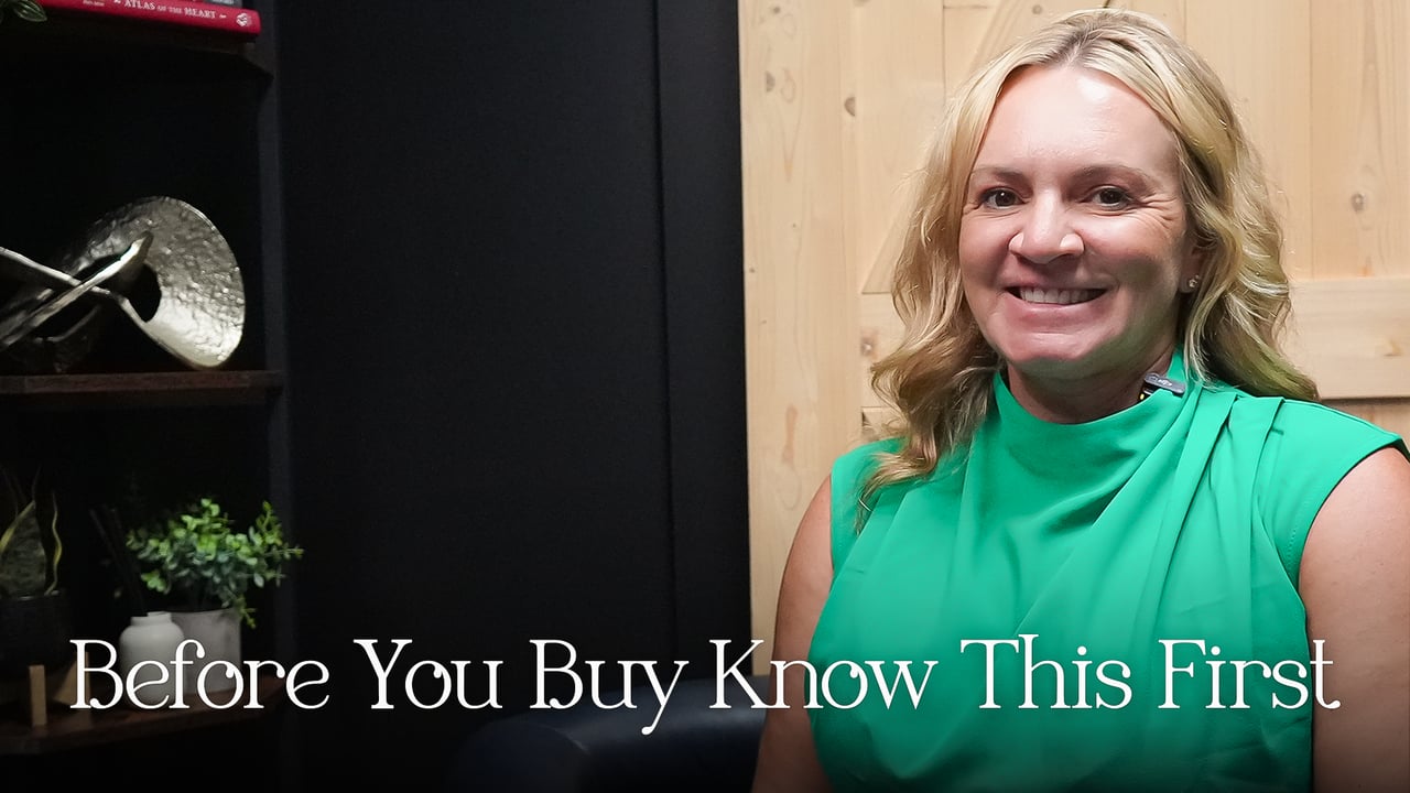 A smiling blonde woman in a green sleeveless top beside a dark display shelf.