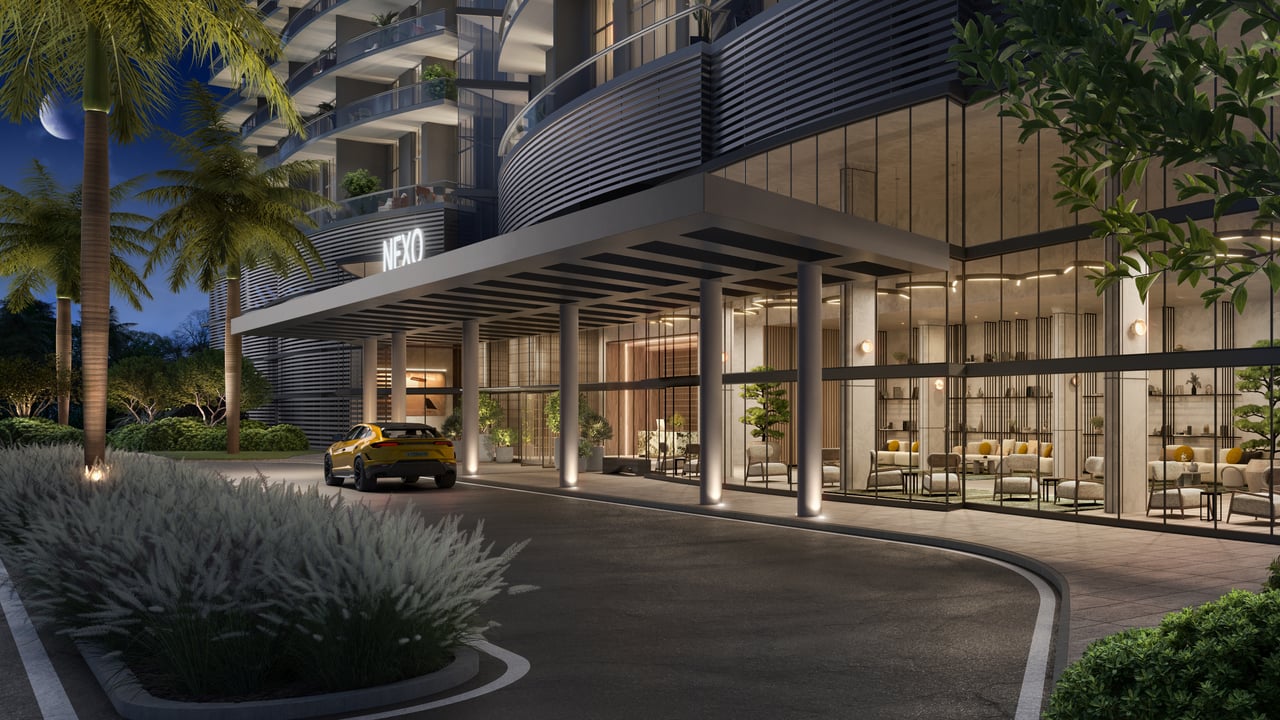 NEXO Residences entrance with a curved facade, glass lobby, palm trees, and a yellow car.