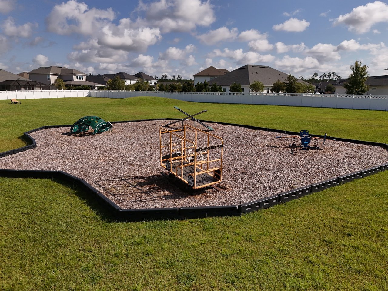 Neighborhood playground with a school-bus-shaped climbing structure, green dome climber, and grassy surroundings.