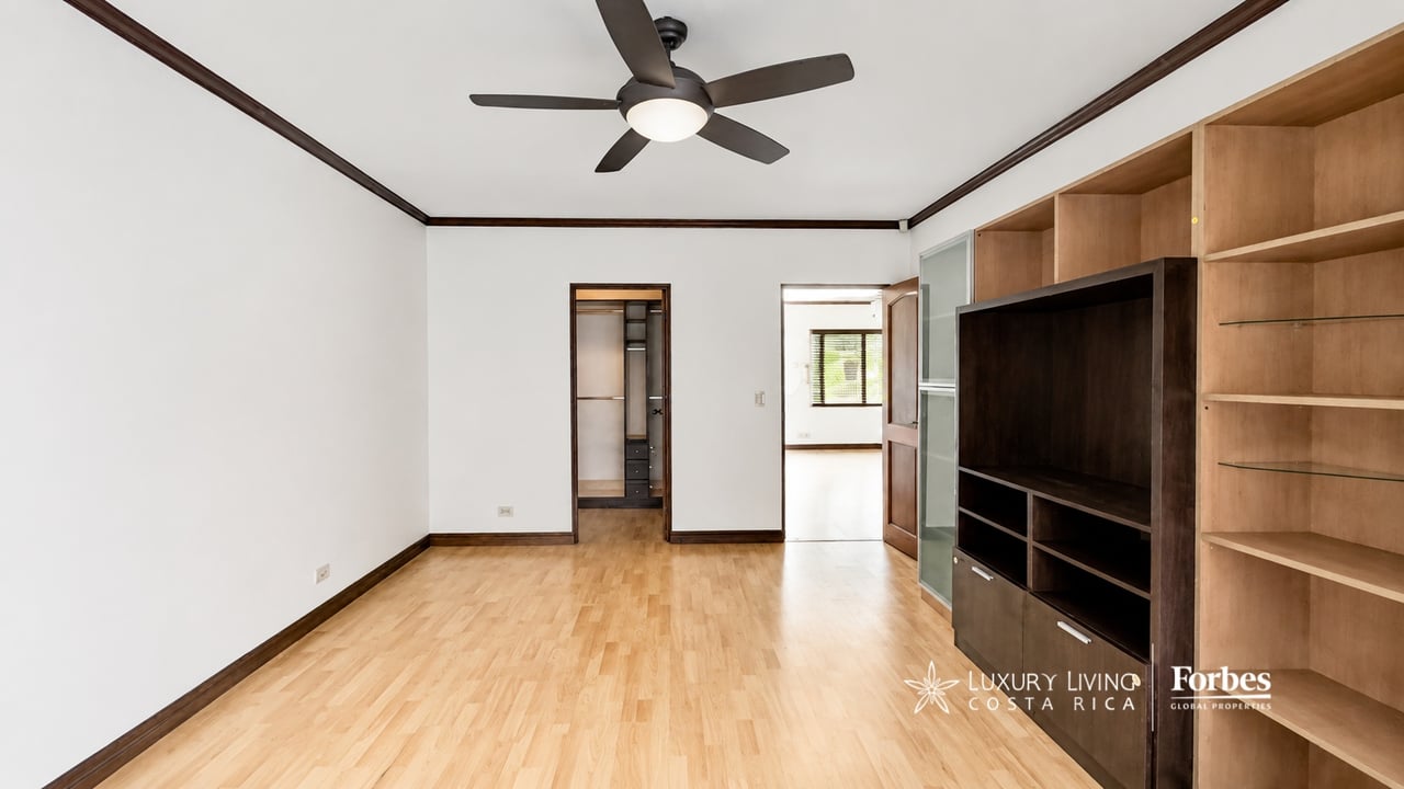 Empty room with wood floors, ceiling fan, and built-in shelving.