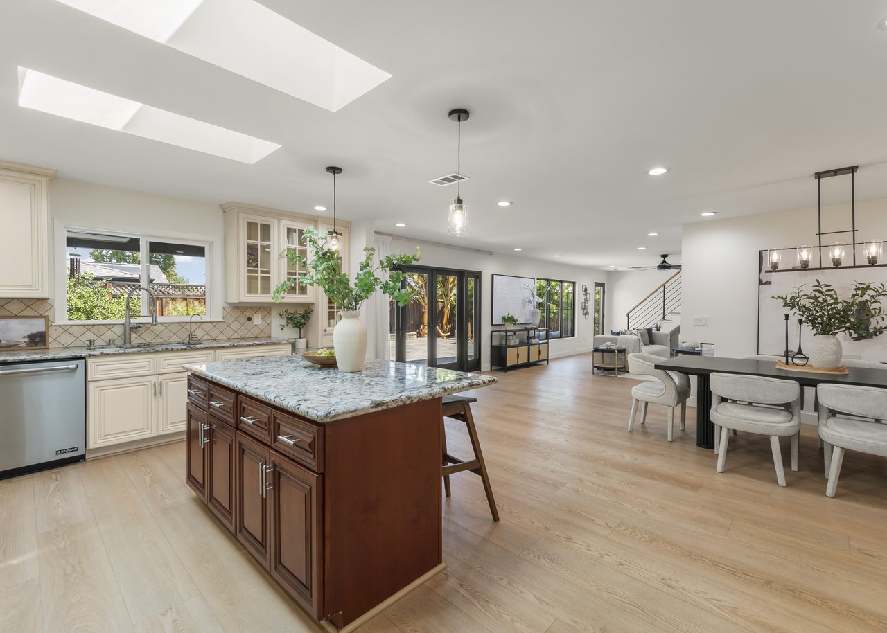 Open-plan kitchen with a large stone-topped island, skylights, dining area, and glass doors to a leafy yard.
