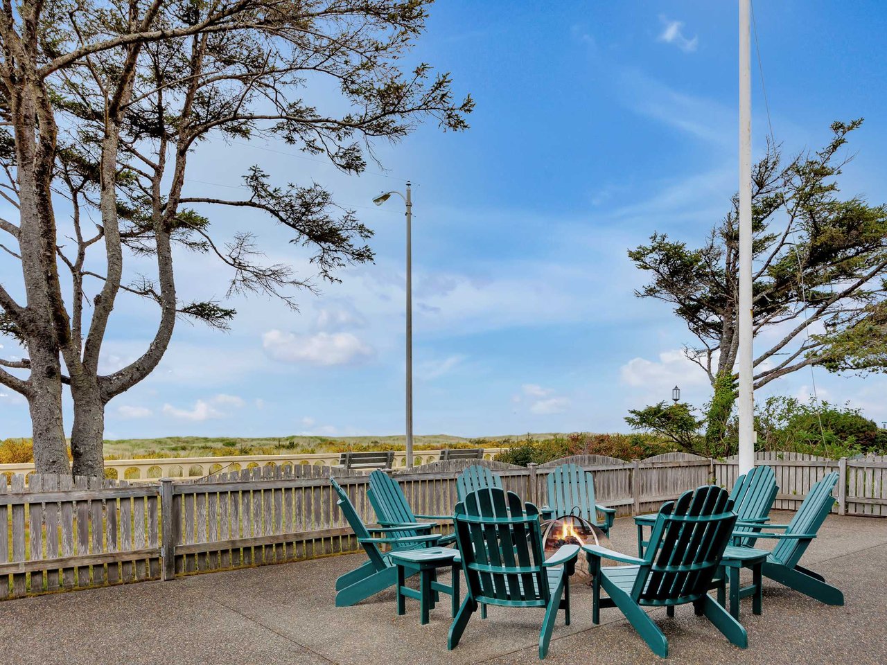 Oceanfront patio on the Oregon Coast featuring Adirondack chairs around a fire pit, coastal dune views, and direct beach access in a peaceful seaside setting