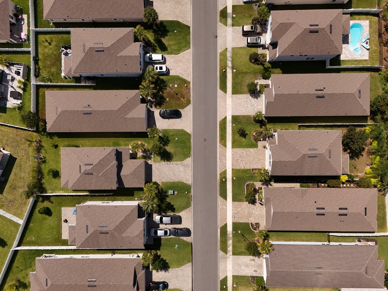 Aerial view of homes along a residential street, with lawns, driveways, and a backyard pool.