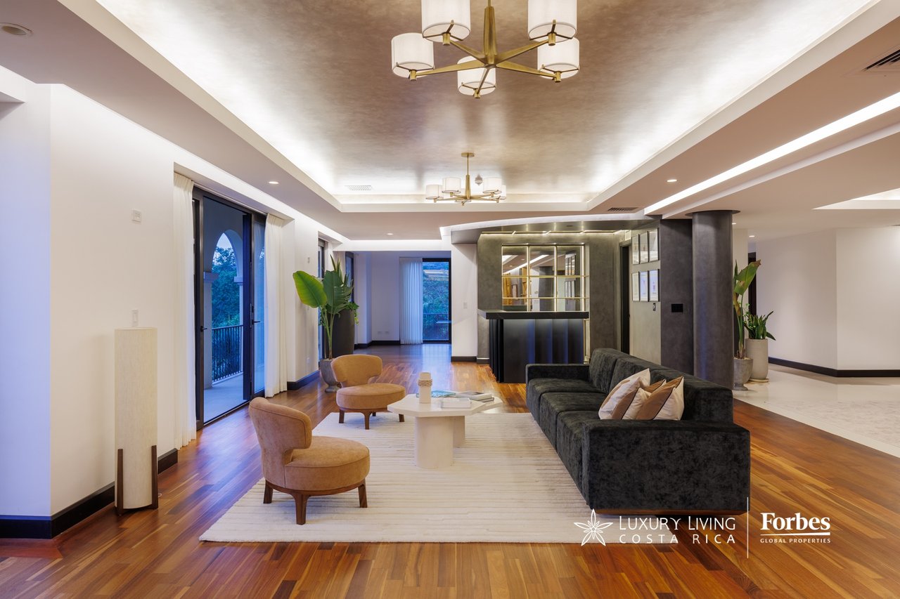 Penthouse living room with a dark sectional, tan lounge chairs, and balcony doors.