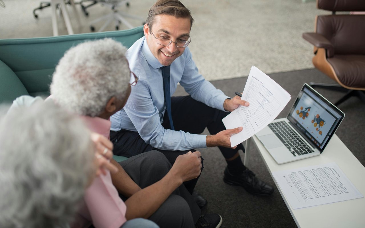 Man reviews paperwork with an older woman beside a laptop and documents.