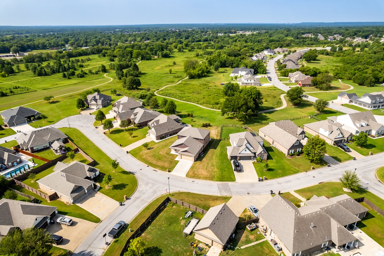 Aerial view of a suburban neighborhood with detached homes, curving streets, and surrounding green fields.