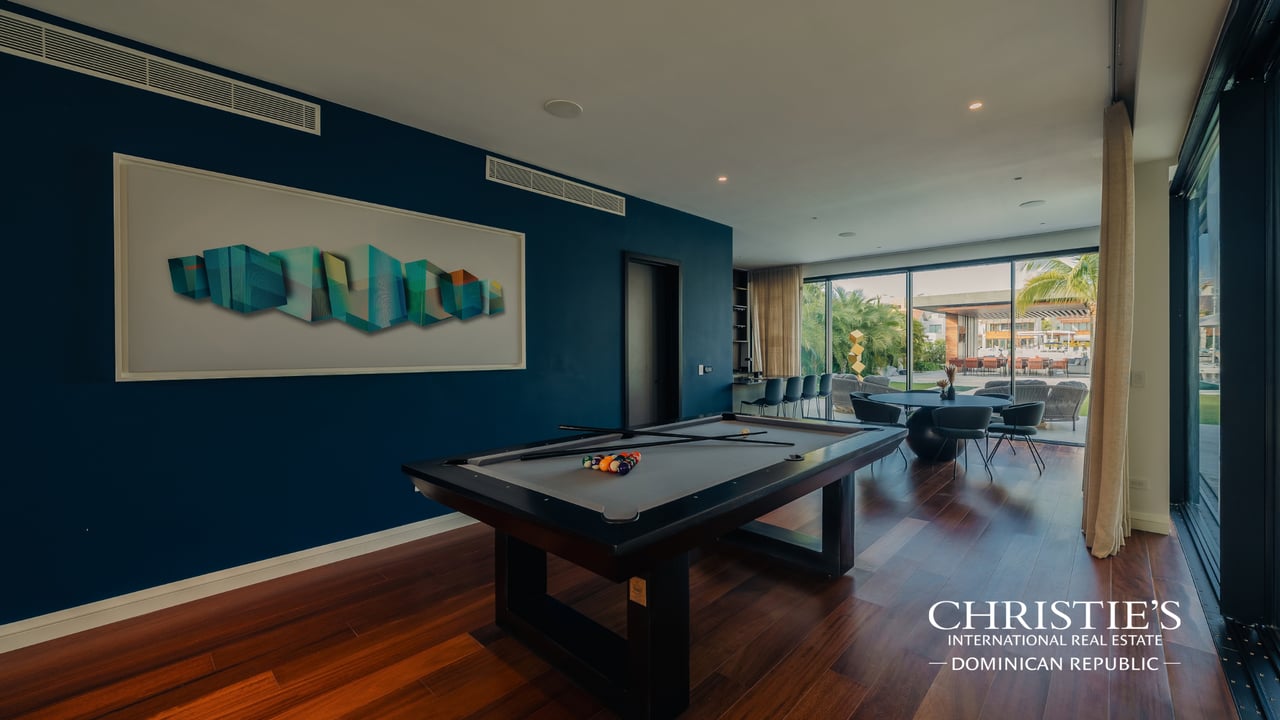 Billiard room with a pool table, teal accent wall, and glass doors opening to a tropical patio.