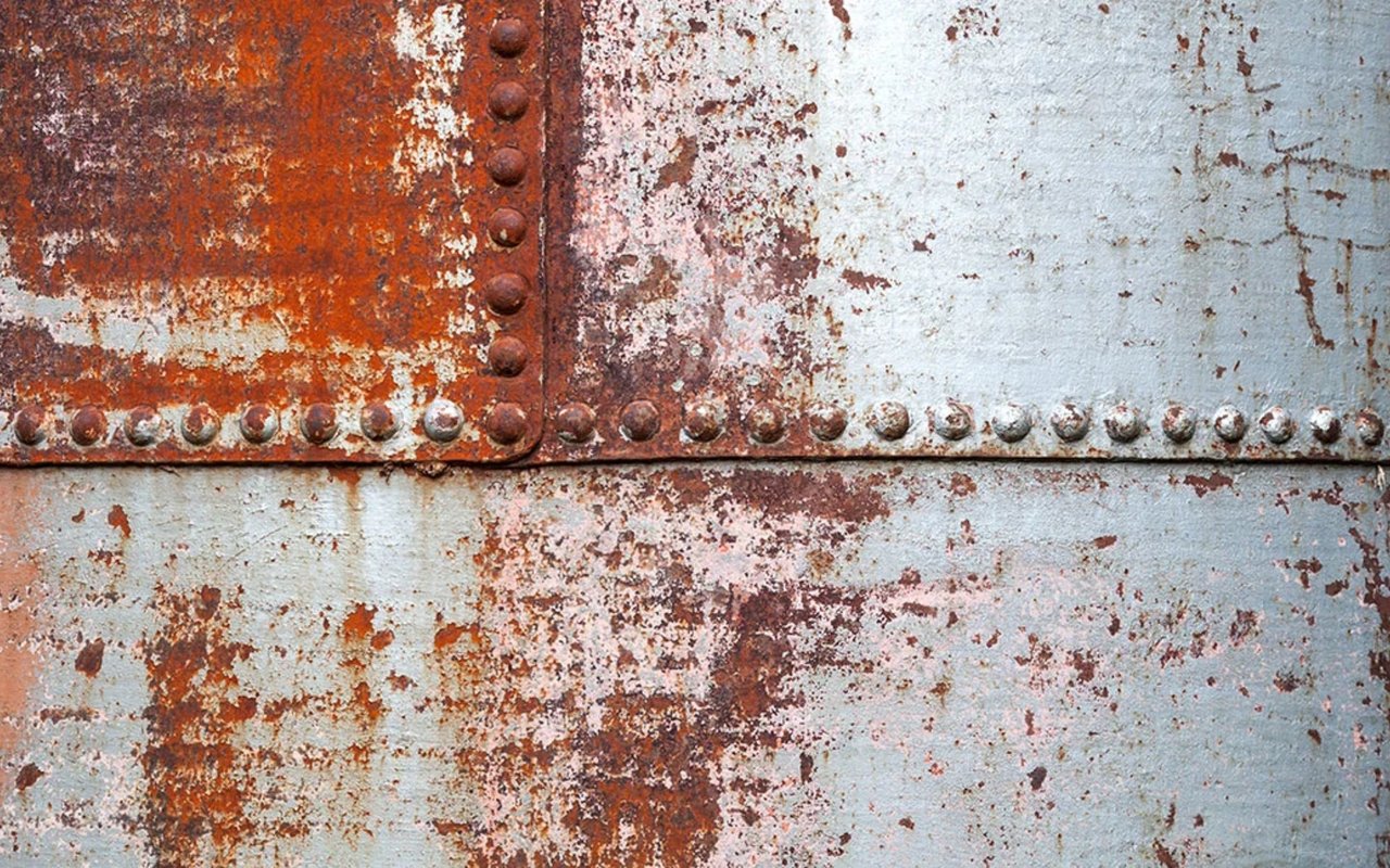 Rusted metal plates with rows of rivets and mottled blue-gray paint.