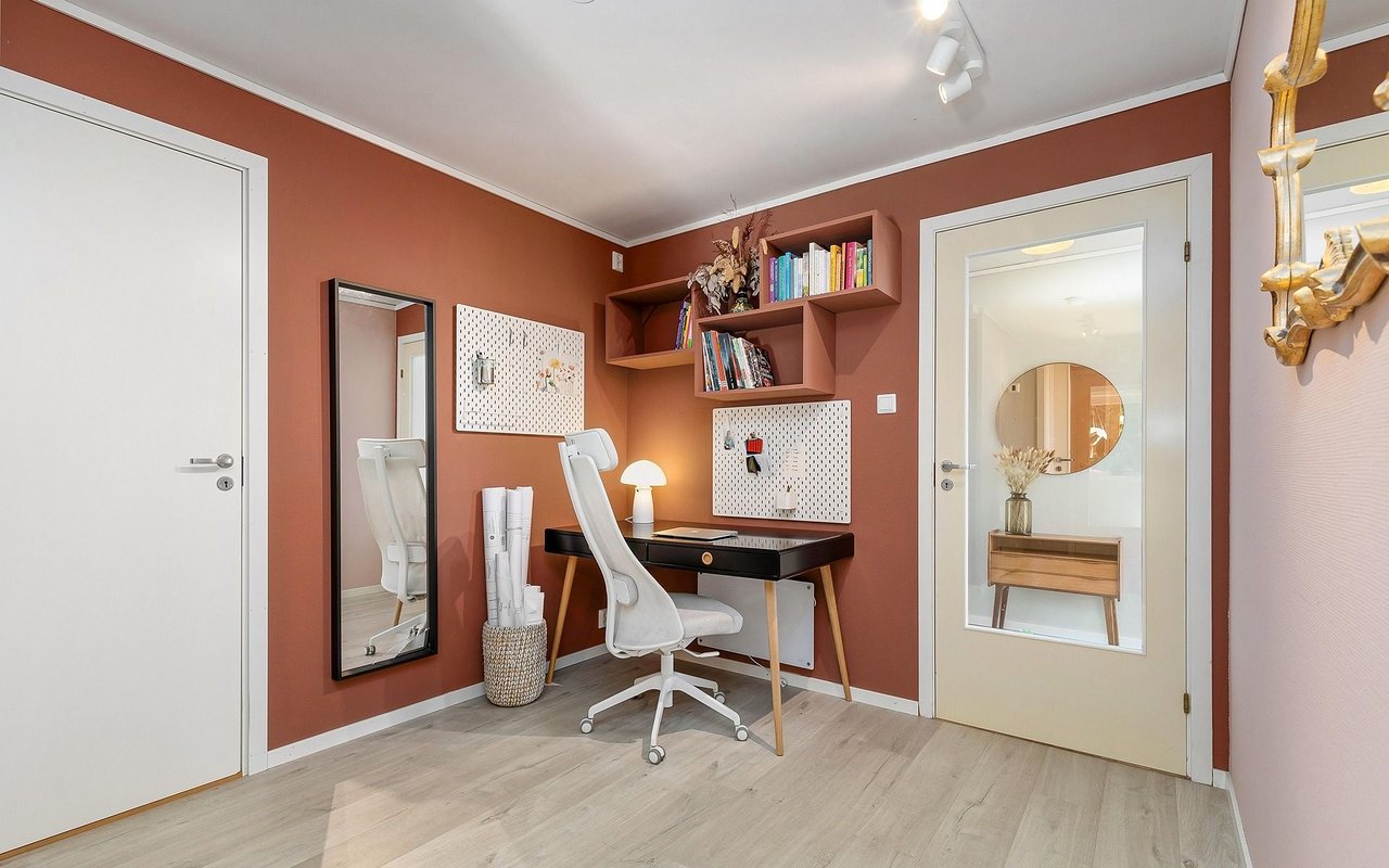 Home office with rust-colored walls, a black desk, white chair, and built-in shelves.