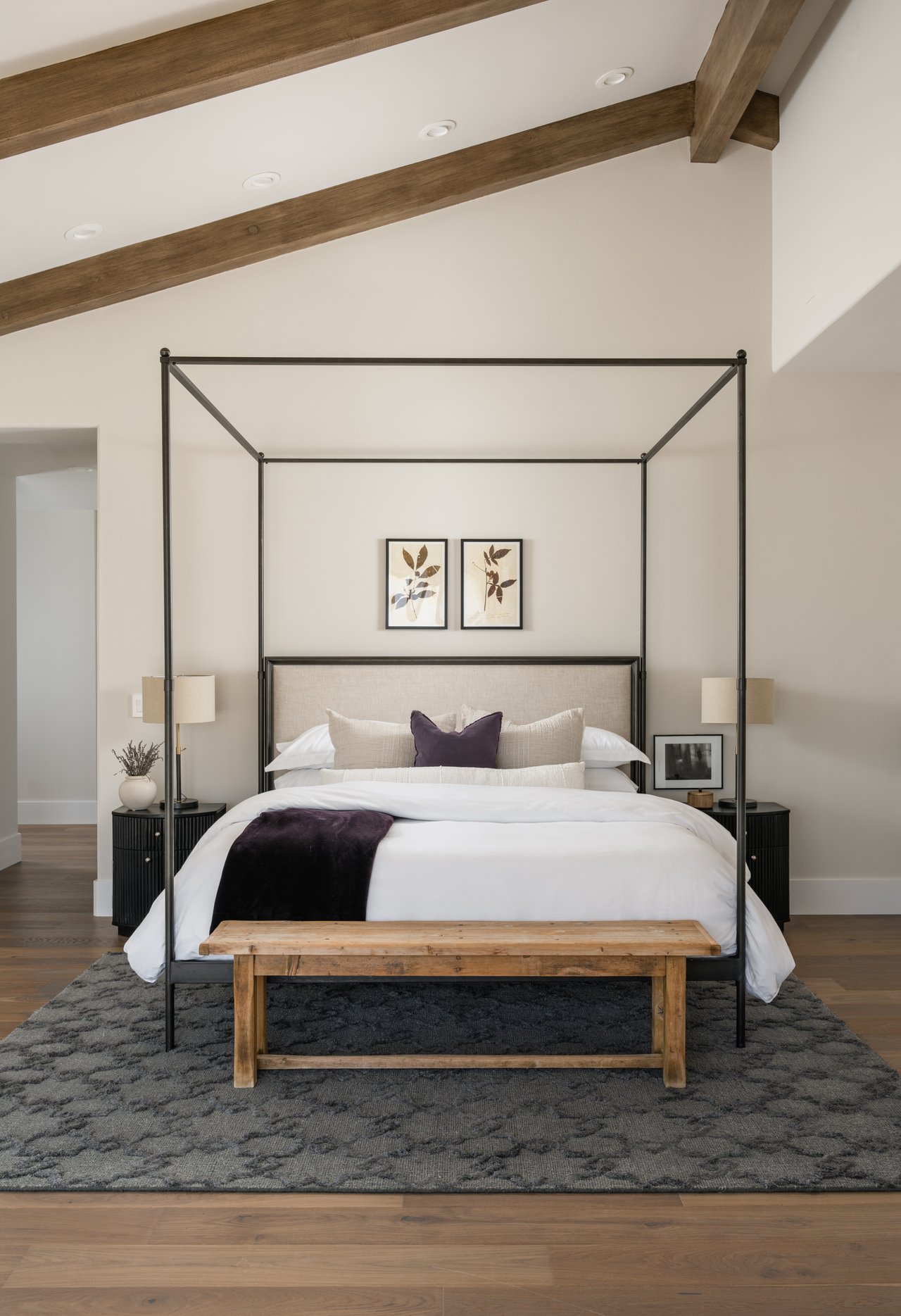 Staged bedroom with a black four-poster bed, exposed wooden beams, and a wooden bench.