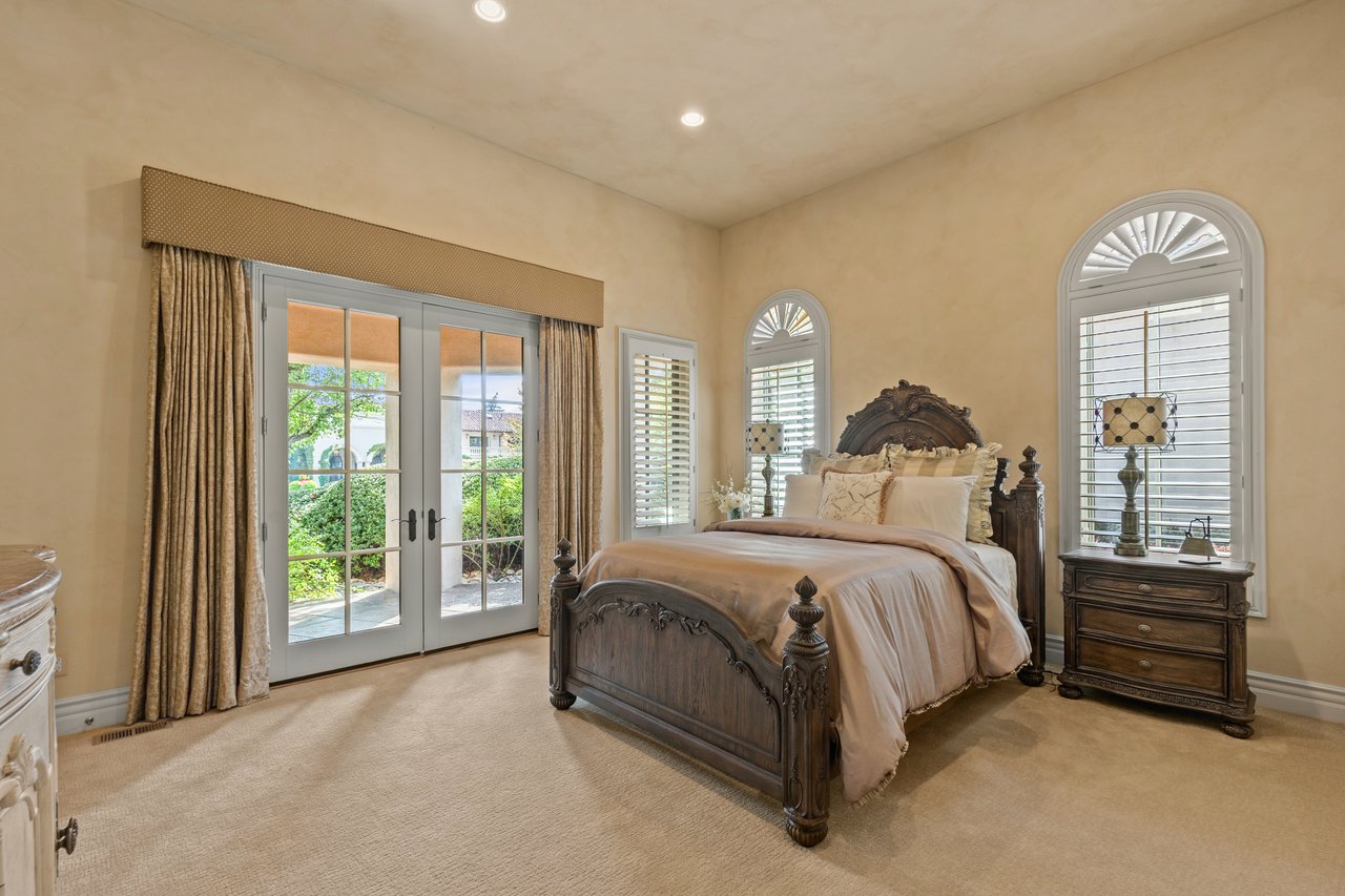 Guest bedroom with a carved wood bed, arched shuttered windows, and garden-facing French doors.