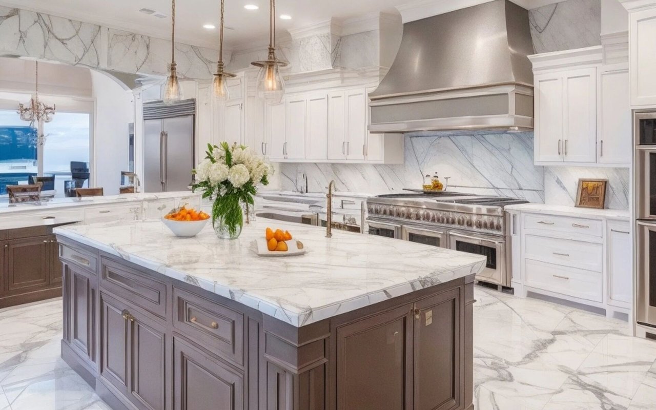Marble kitchen with a large dark island, professional range, pendant lights, and water visible through the window.