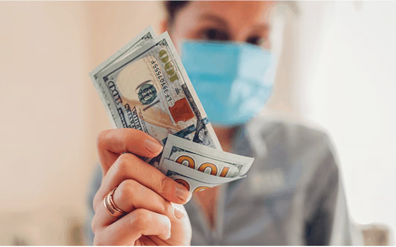 Masked person holding U.S. dollar bills