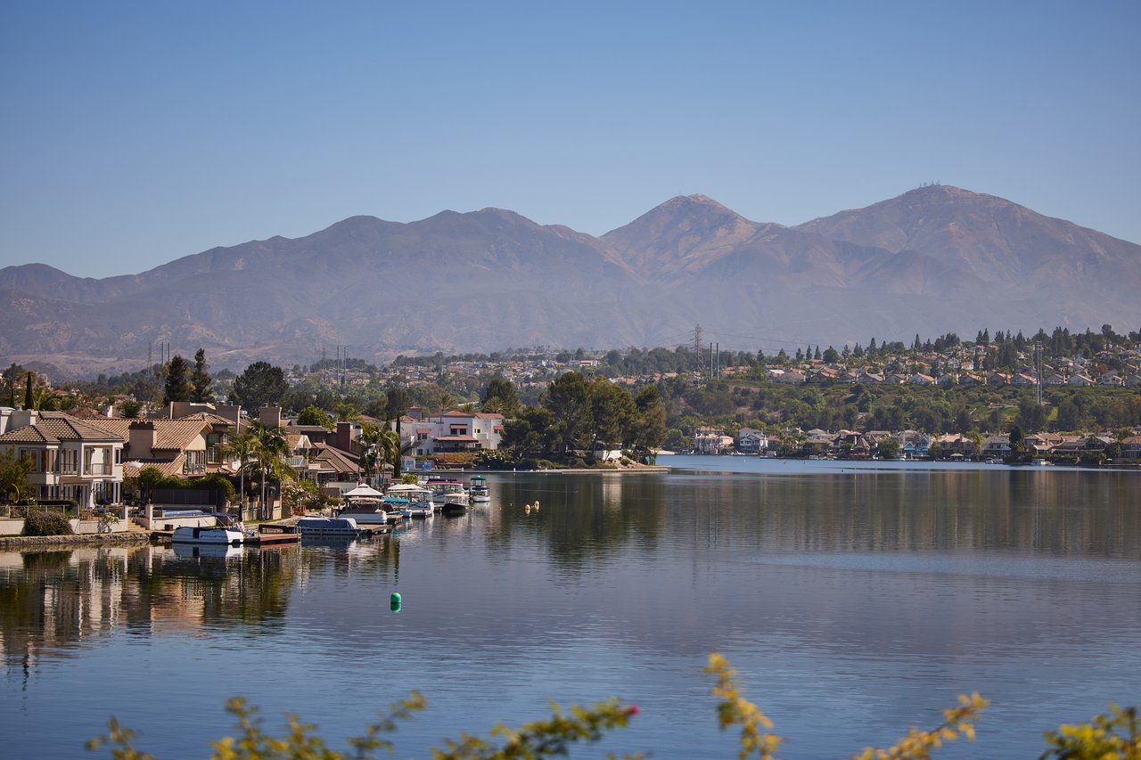 Lake Mission Viejo with lakefront homes along the far shore and the Saddleback peaks under a clear blue sky