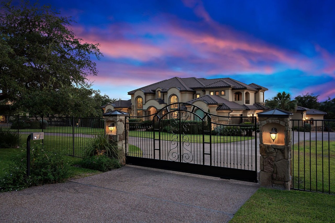 Twilight view of the gated entry with wrought iron gates and stone pillars at 25715 Cliff Circle, Lakecliff on Lake Travis, Spicewood, Texas.